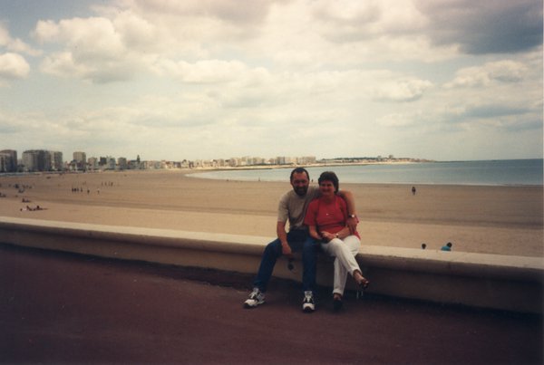 Un homme et une femme assis sur un muret face à une plage.ᴬᴵ