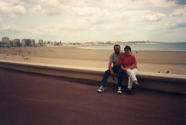 Un homme et une femme assis sur un muret face à une plage.ᴬᴵ