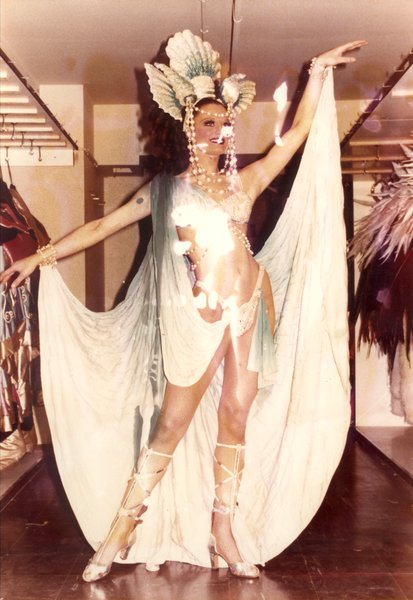 Danseuse de revue, à talons hauts, coiffe et grands voiles.