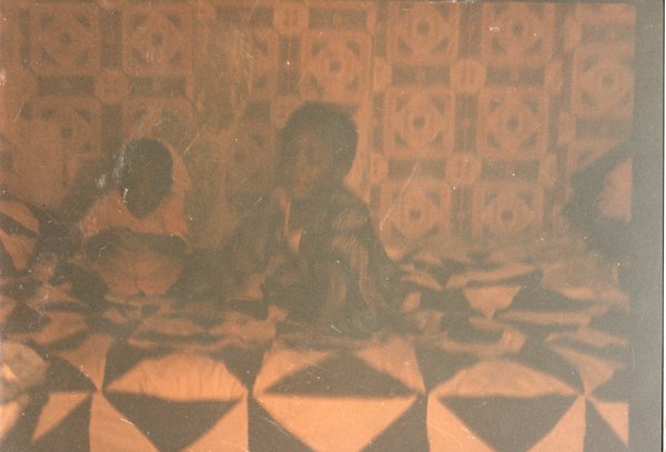 Deux enfants assis sur un lit à couverture à motifs.