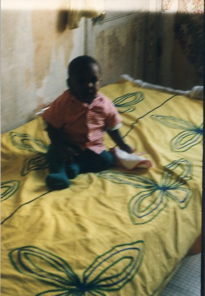 Enfant assis sur un lit à parure jaune.