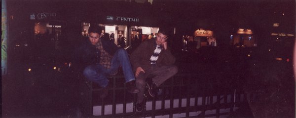 Deux jeunes hommes assis sur une balustrade dans la rue, la nuit.
