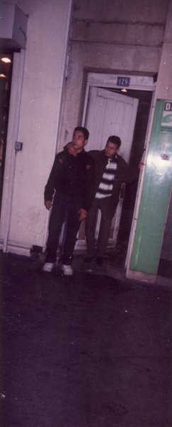 Deux jeunes hommes debout dans l’embrasure d’une porte de nuit.