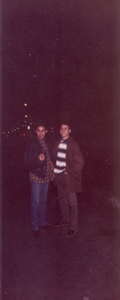 Deux jeunes hommes debout souriant dans la rue de nuit.