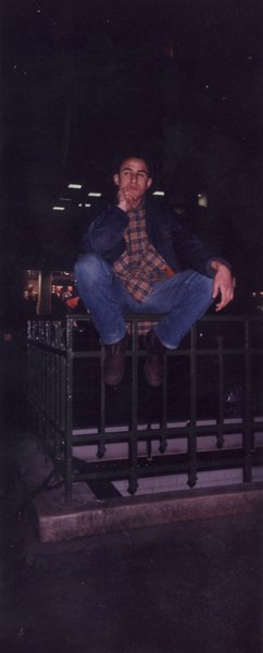 Jeune homme assis sur une balustrade dans la rue, la nuit.
