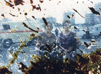 Deux femmes debout souriantes devant un front de mer et des immeubles. Image avec traces de brûlures.
