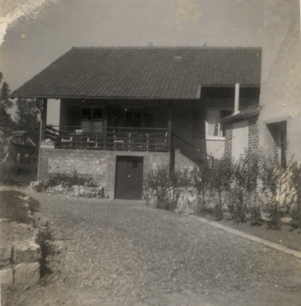 Maison au bout d’une allée bordée d’arbustes. Noir et blanc.