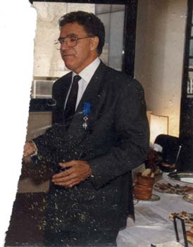 Homme debout en complet où est épinglée une décoration devant un buffet de cocktail.