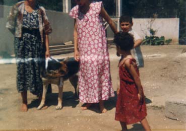 Femmes pieds nus en robes à fleurs avec une petite fille brune, un petit garçon, et un chien.