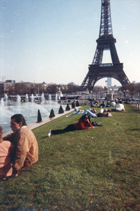Femme en rouge et lunettes de soleil allongée sur la pelouse du jardin du Trocadéro, la Tour Eiffel en arrière-plan.