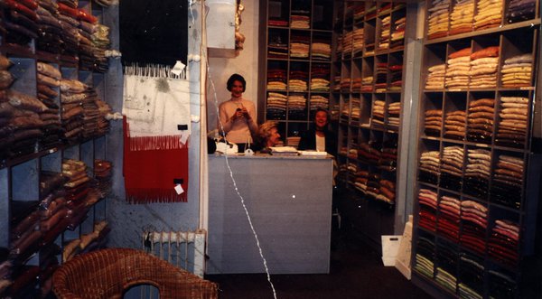 Intérieur d'un magasin de vêtements avec étagères de pulls pliés et trois personnes.ᴬᴵ