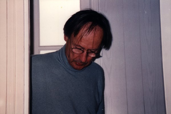 Homme à lunettes regardant vers le bas dans l'encadrement d'une porte.ᴬᴵ