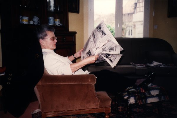 Femme âgée lisant un journal assise dans un fauteuil.ᴬᴵ