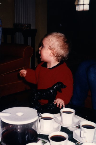 Bébé aux cheveux blonds en pull rouge assis devant des tasses de café.ᴬᴵ