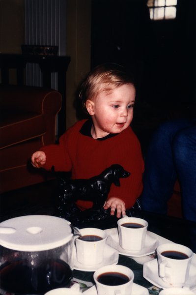 Enfant en pull rouge près de tasses de café et d'une figurine de chien noir.ᴬᴵ