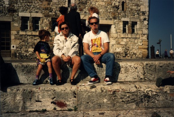 Deux hommes, une femme et un enfant assis sur un rempart, tous en lunettes de soleil.ᴬᴵ