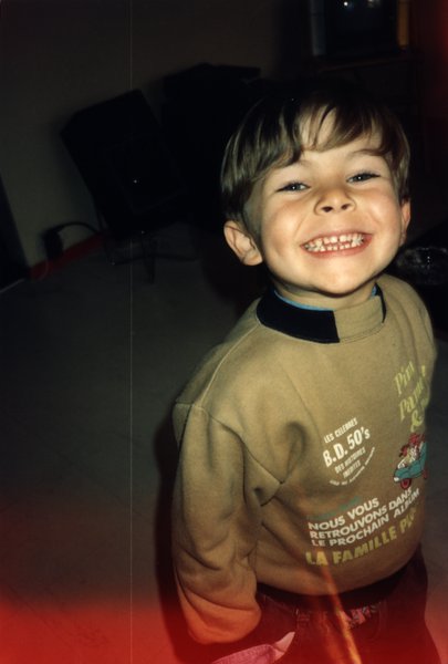 Enfant souriant largement en sweat marron, photo avec halo de lumière rouge.ᴬᴵ