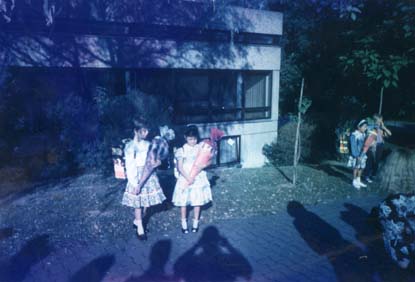 Petites filles en jupes fleuries debout devant un pavillon, des pochettes surprises dans les bras.