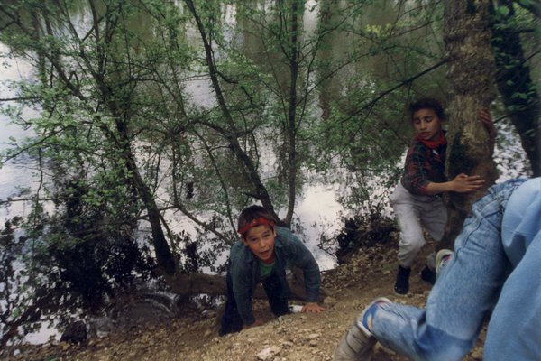 Jeunes garçons grimpant une pente, plan d’eau en arrière-plan.