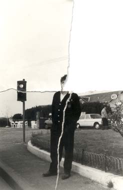 Homme brun debout devant un feu de croisement dans la rue.
