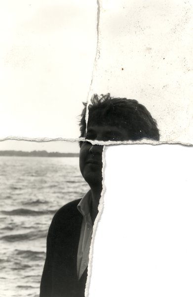 Visage d’homme brun, la mer en arrière-plan. Noir et blanc. Image déchirée en partie reconstituée.