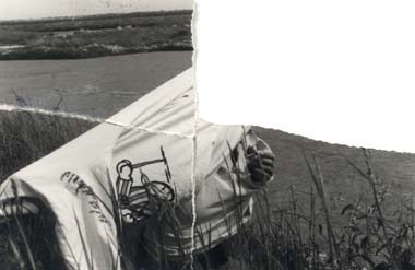 Individu en train d’enlever un tee-shirt, plan d’eau en arrière-plan. Image déchirée en partie reconstituée. Noir et blanc.