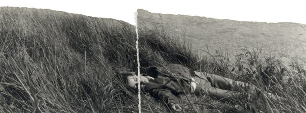 Individu allongé dans de grandes herbes. Image déchirée en partie reconstituée. Noir et blanc.