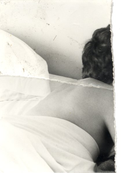 Dos de femme nu dans un lit. Image déchirée en partie reconstituée. Noir et blanc.