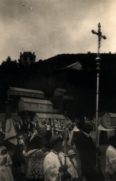 Procession religieuse avec croix portée en tête, cabines de plage en arrière-plan. Photo ancienne sépia.ᴬᴵ