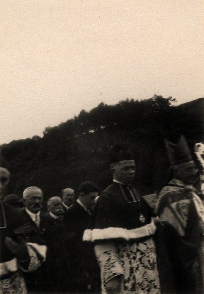 Clergé et hommes rassemblés devant une colline lors d'une procession. Photo ancienne sépia.ᴬᴵ