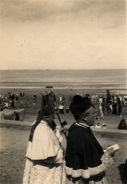 Évêque en mitre et clergyman regardant une plage bondée. Photo ancienne sépia.ᴬᴵ