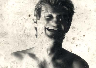Homme torse nu avec des yeux clairs riant aux éclats. Noir et blanc.