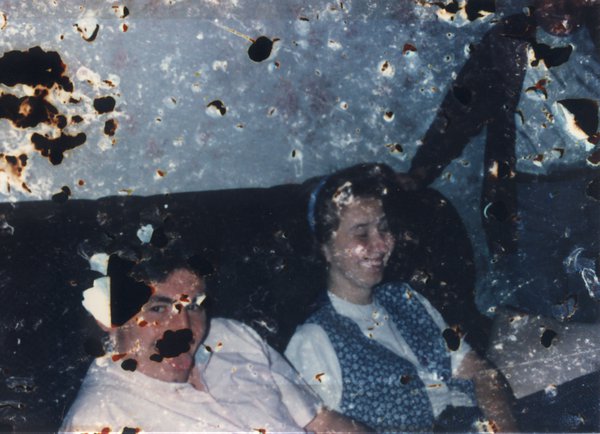 Homme rubicond et femme brune souriante sur un canapé. Image très abîmée.