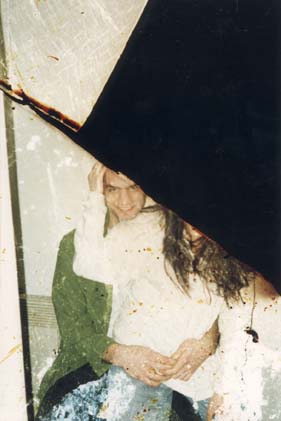 Femme brune assise sur les genoux d’un jeune homme en veste verte souriant. Image avec brûlures.