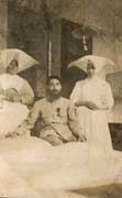 Homme barbu en uniforme assis entre deux bonnes sœurs à cornettes. Noir et blanc.