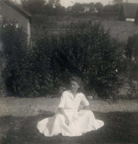 Femme en robe blanche assise au milieu d’une pelouse. Noir et blanc.