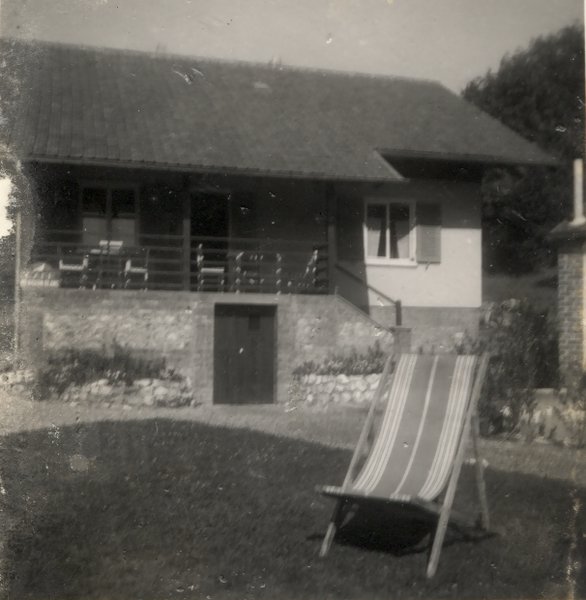 Transats sur une pelouse devant une maison de type chalet. Noir et blanc.