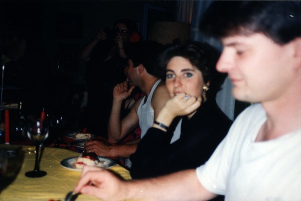 Convives attablés lors d'un dîner, une personne prenant une photo en arrière-plan.ᴬᴵ