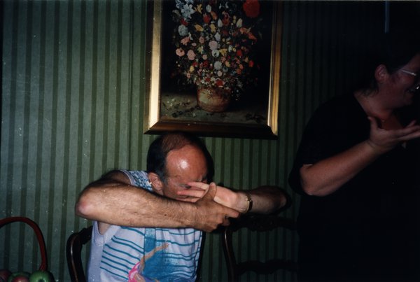 Homme se cachant le visage avec le bras, assis sous un tableau de fleurs.ᴬᴵ