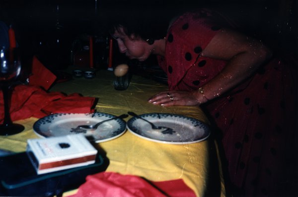 Femme en robe à pois rouge penchée au-dessus d'une table lors d'un jeu de soirée.ᴬᴵ
