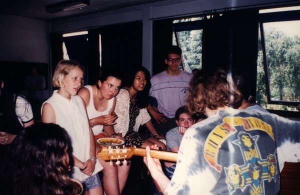 Groupe d'adolescents réunis autour d'un jeune homme jouant de la guitare.ᴬᴵ