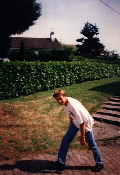 Adolescent penché en avant sur un chemin pavé, devant une haie et une maison.ᴬᴵ