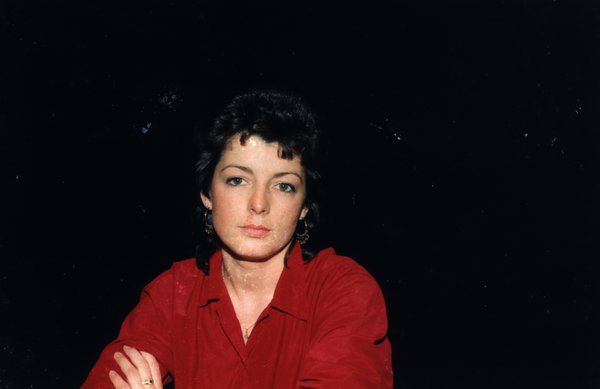 Portrait de femme en haut rouge à l'expression sérieuse, fond sombre.ᴬᴵ
