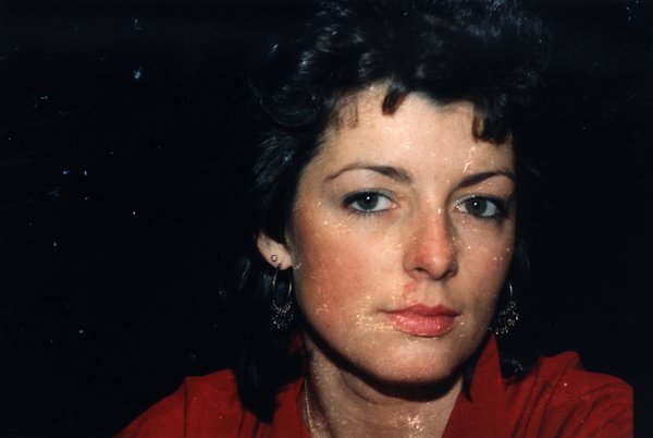 Gros plan du visage d'une femme en haut rouge, fond sombre.ᴬᴵ