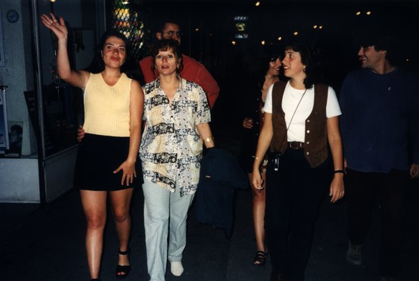 Groupe marchant dans une rue de nuit, une femme faisant signe de la main.ᴬᴵ