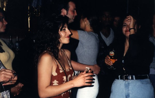 Femme souriante lors d'une soirée dans un bar, entourée d'autres personnes.ᴬᴵ