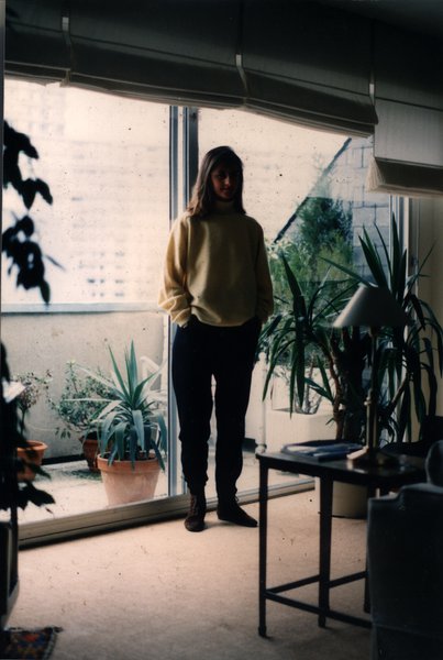 Jeune homme debout près d'une baie vitrée avec des plantes, vue sur la ville.ᴬᴵ