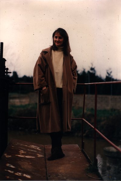 Femme en long manteau debout sur une passerelle au bord d'un canal.ᴬᴵ