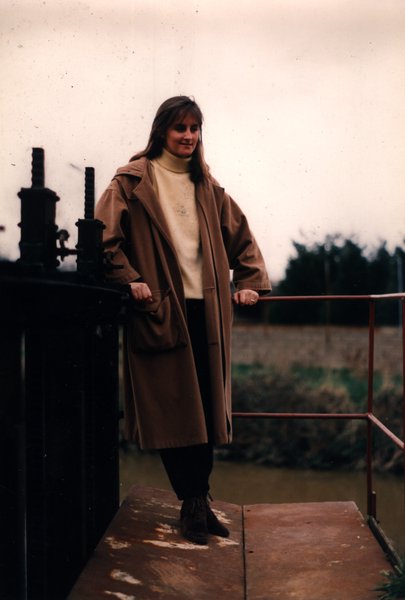 Femme en manteau beige souriante près d'une écluse.ᴬᴵ