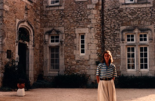 Femme en chemise rayée devant la façade en pierre d'un château.ᴬᴵ